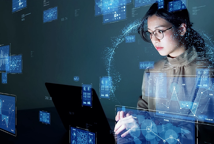 A woman wearing glasses focuses on a laptop screen displaying a digital interface.