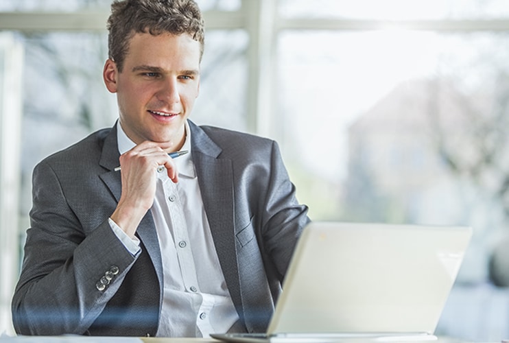 A professional man in a suit sits at a desk, focused on his laptop.